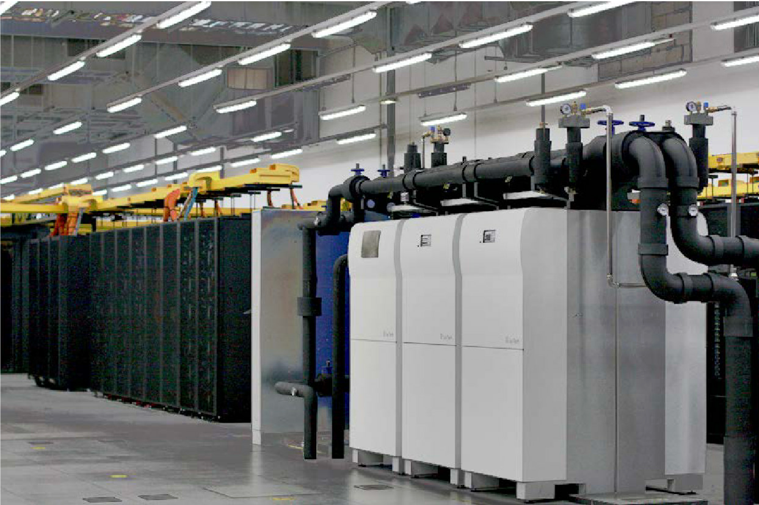 Image of the CoolMUC-2 computer racks (black racks) and six adsorption chillers powered by waste heat from the computer racks (light gray devices on the right side of the image).